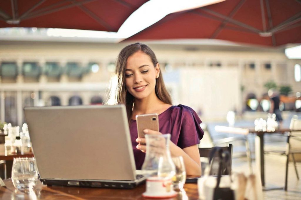 Woman reading phone while looking at laptop in cafe